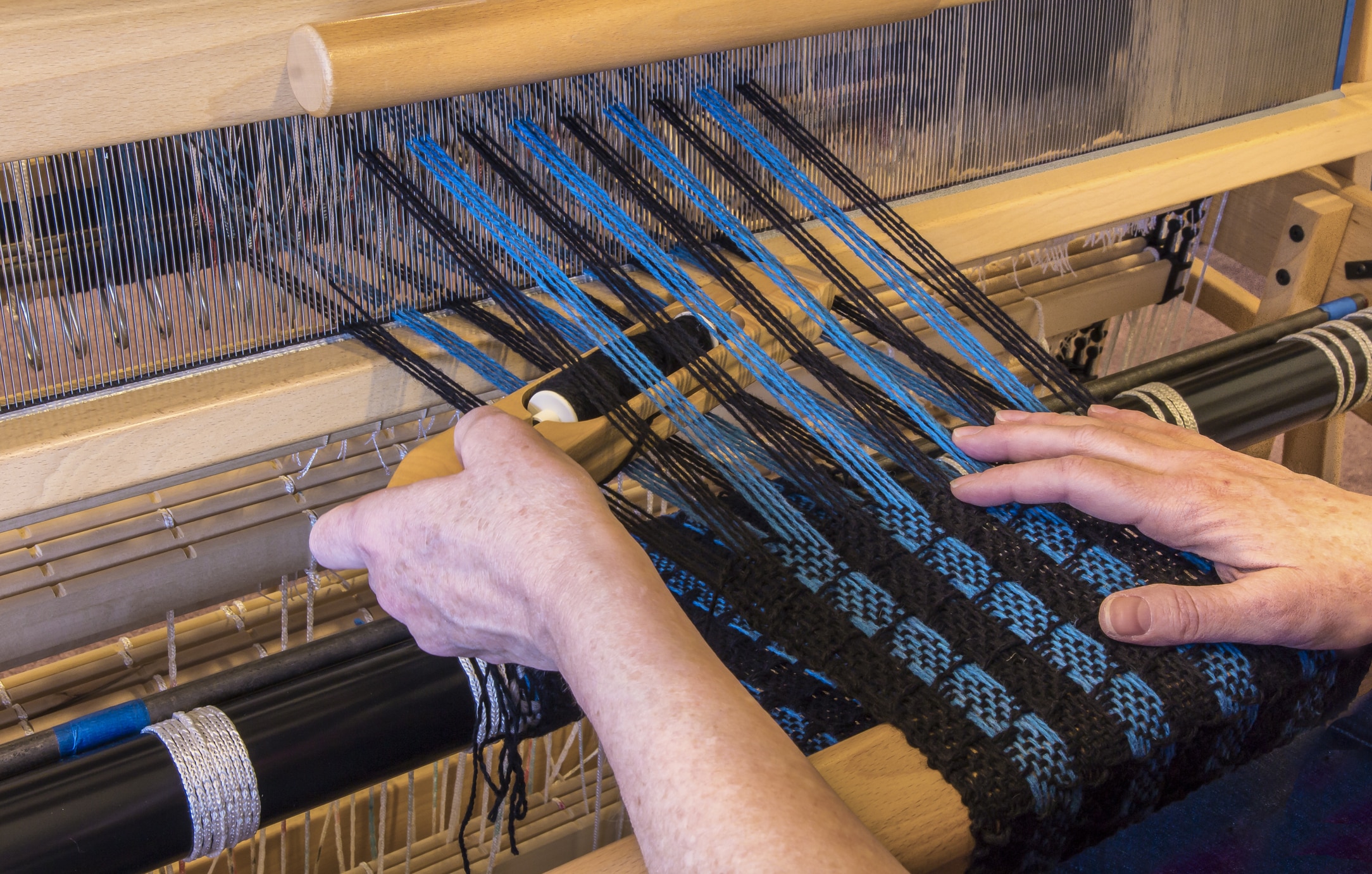 Woman weaving a wool scarf on a floor loom.